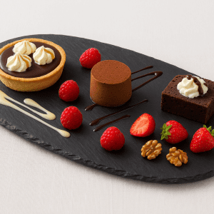 Bandeja ovalada de pizarra natural de 40 × 22 cm con postres variados presentada sobre una mesa con mantel blanco