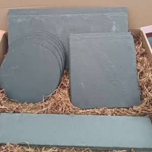 Pack de platos y bandejas de pizarra natural en diferentes formatos presentados en caja, ideales para servir aperitivos, carnes y postres