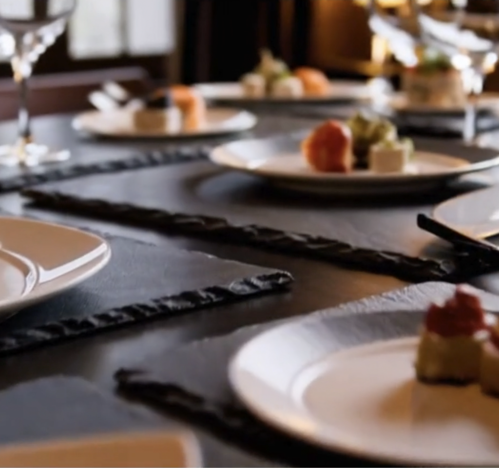 Bajo plato de pizarra natural con vajilla de cerámica blanca encima, ideal para presentación en catering y restaurantes