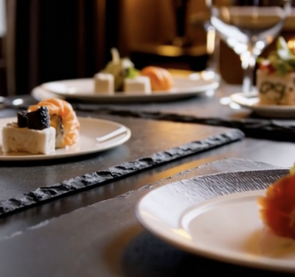 Bajo plato de pizarra natural con vajilla de cerámica blanca encima, ideal para presentación en catering y restaurantes